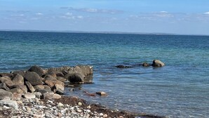 En kustvy med en stenig strand, ett lugnt hav och land i fjärran.