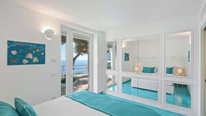 Ein Schlafzimmer mit Bett, Meerblick, einem Balkon und einem Badezimmer mit Spiegel.