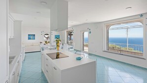 Eine moderne Küche mit einer großen Kochinsel, weißen Schränken und Meerblick durch ein großes Fenster.