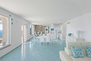 A bright living room with a dining area, a kitchen, and a view of the sea. - AMORE RENTALS-Villa Lantana-Nature Oasis with Panoramic Jacuzzi near Amalfi (Massa Lubrense)