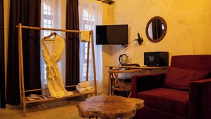 Une pièce comprenant un présentoir en bois sur lequel est posée une serviette blanche, un fauteuil rouge, une petite table en bois avec une bouilloire, un téléviseur et un miroir fixé au mur.
