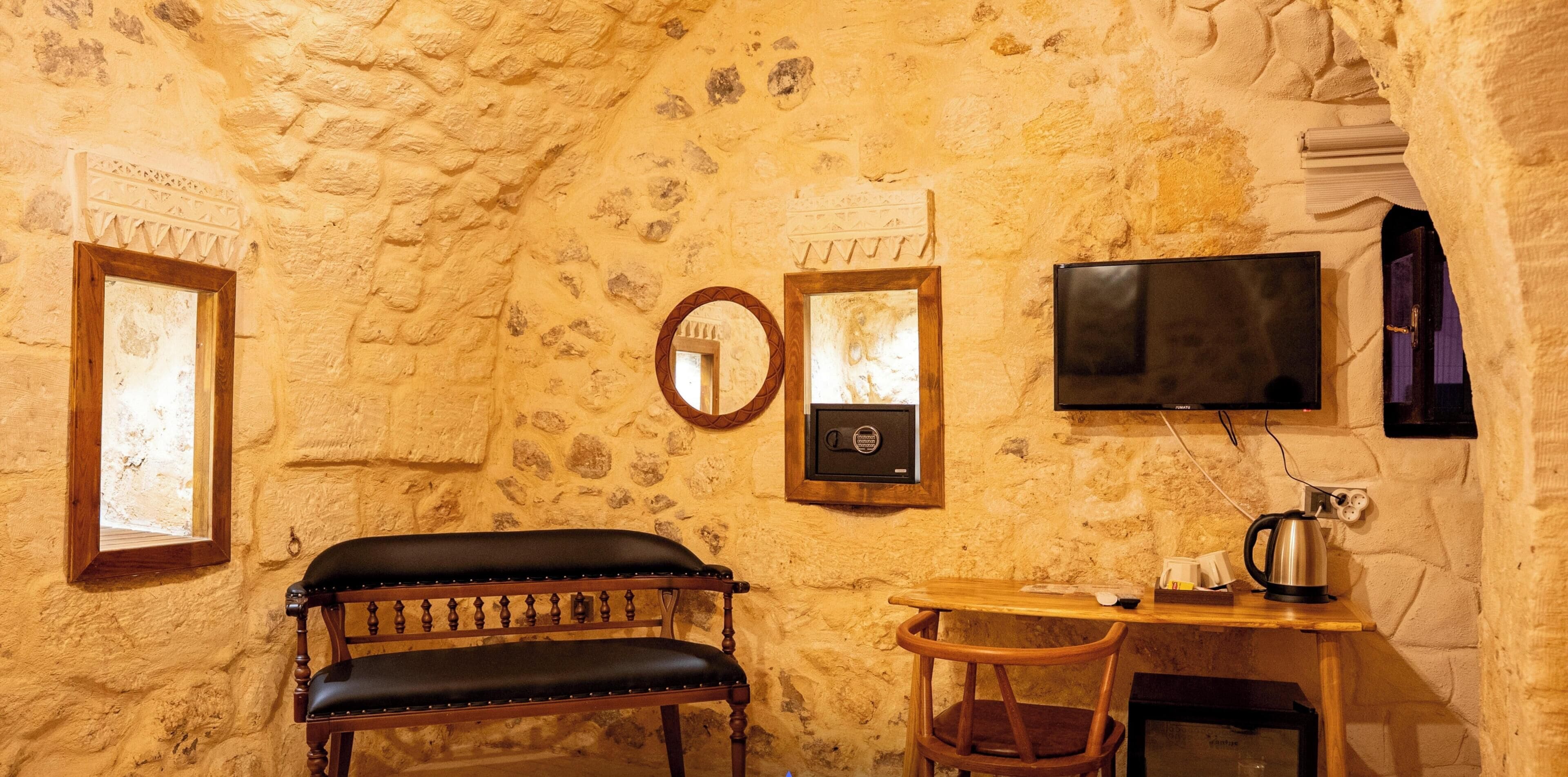 Ein rustikaler Raum mit Steinwand, einer hölzernen Bank, einem kleinen Tisch mit Stuhl, einem Fernseher und einer Kaffeemaschine.