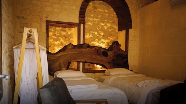 Une chambre rustique avec un mur en pierre, un plafond en bois et un lit recouvert de linge de lit blanc.