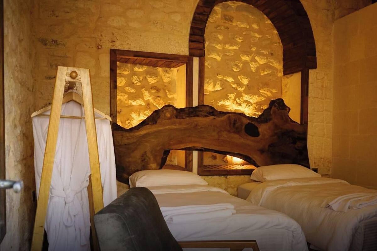 Quarto rústico com parede de pedra, teto de madeira e cama com roupa de cama branca.