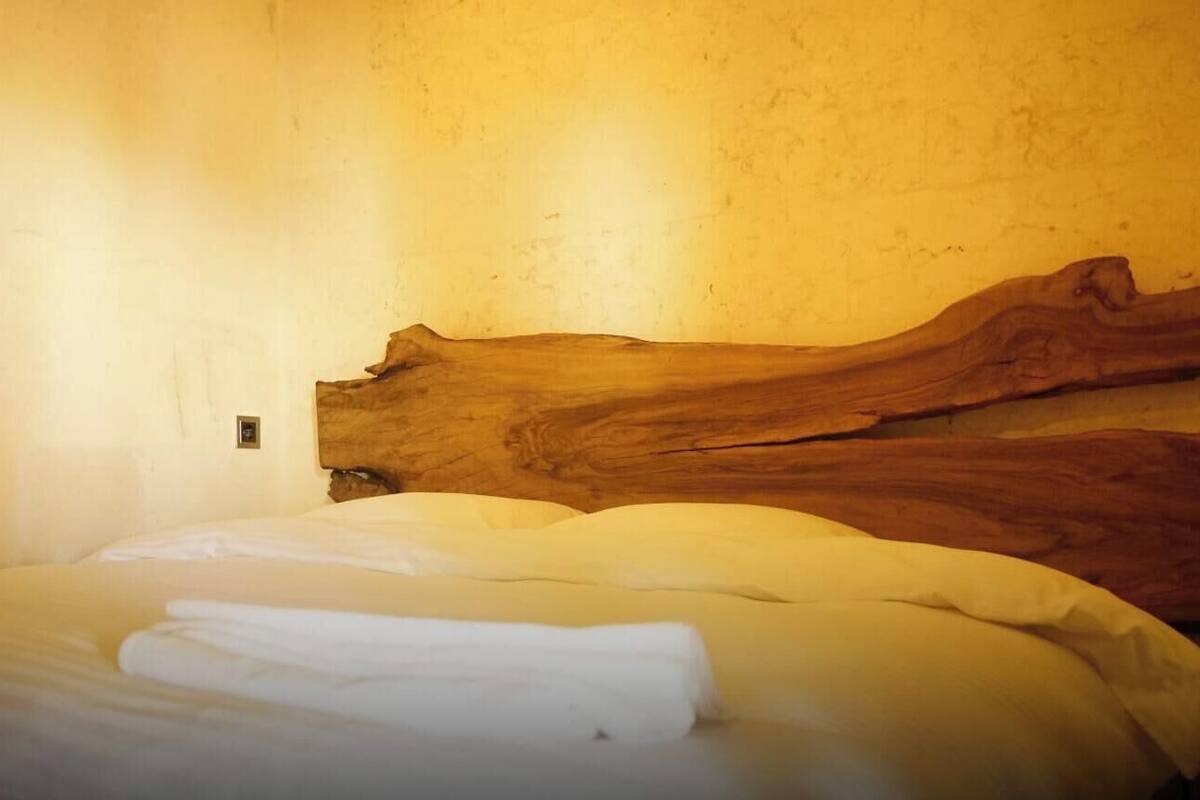 Uma cama com roupa de cama branca, cabeceira de madeira e parede com textura.