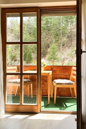 Eine Holztür mit Schiebetürfunktion führt zu einem Außenbereich mit Sitzgelegenheit und Blick auf einen Wald.
