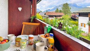 En balkon med et bord dækket til morgenmad, inklusive en skål med frugt, en kop, en appelsinjuiceflaske og forskellige spiser.