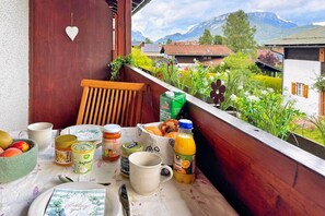 Ein Balkon mit einem Tisch, gedeckt für das Frühstück, darunter eine Obstschale, eine Tasse, eine Orangensaftflasche und verschiedene Speisen.