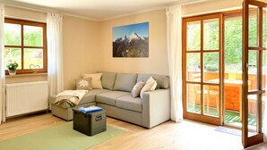 En stue med sofa, radiator, et vindue og en dør, der fører til et udendørs område.