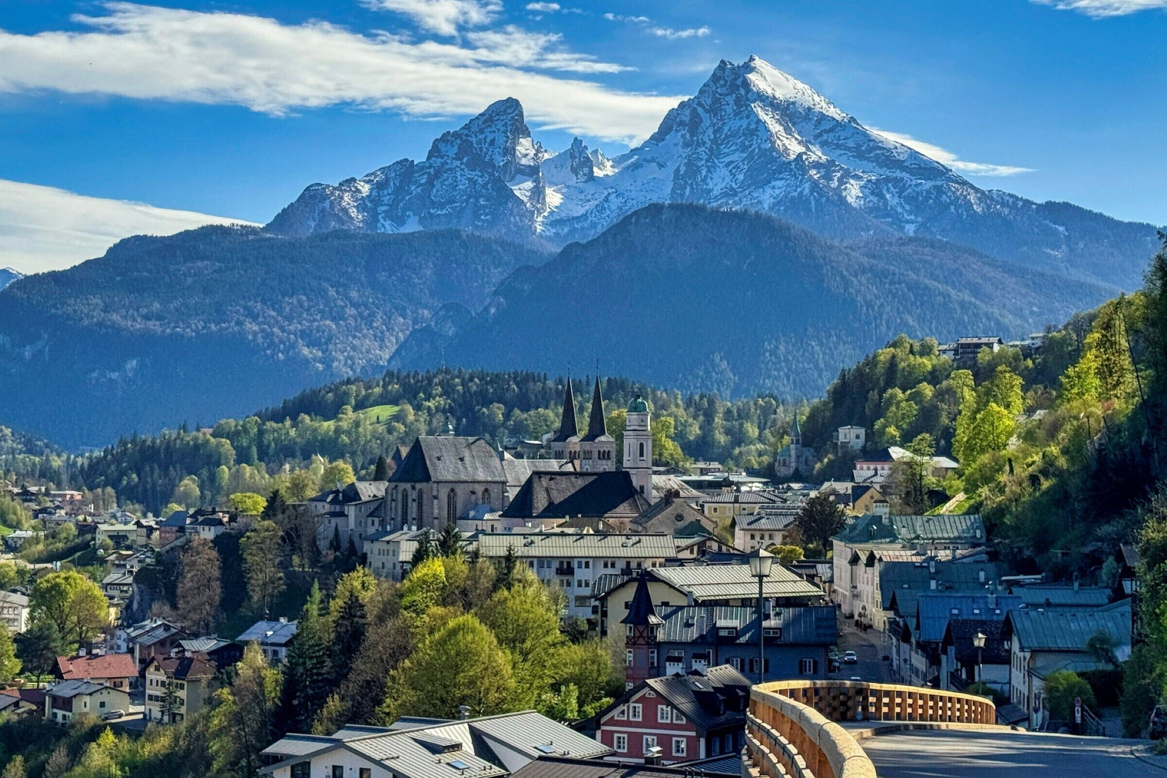 A town with historic buildings, a prominent church, and snow-capped mountains in the background.