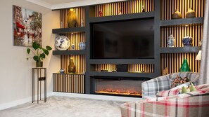 A living room with a fireplace, a flat-screen TV, and decorative shelves. - Sandford House - Townhouse in Regency Cheltenham, Sleeps 8 (Cheltenham)