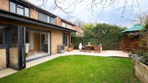 Een modern huis met een glazen deur, een terras met een tafel en stoelen, en een verzorgd gazon.