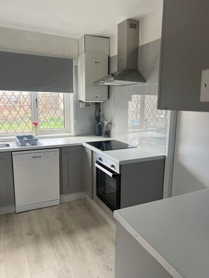 Eine moderne Küche mit grauen Schränken, einem Geschirrspüler, einem Backofen und einem Fenster mit Blick auf einen Garten.