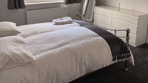 A bedroom with a bed, a dresser, a window with curtains, and a radiator. - Modern Comfort Home | Relax & Unwind in our 4 bed family friendly. (Oxford)