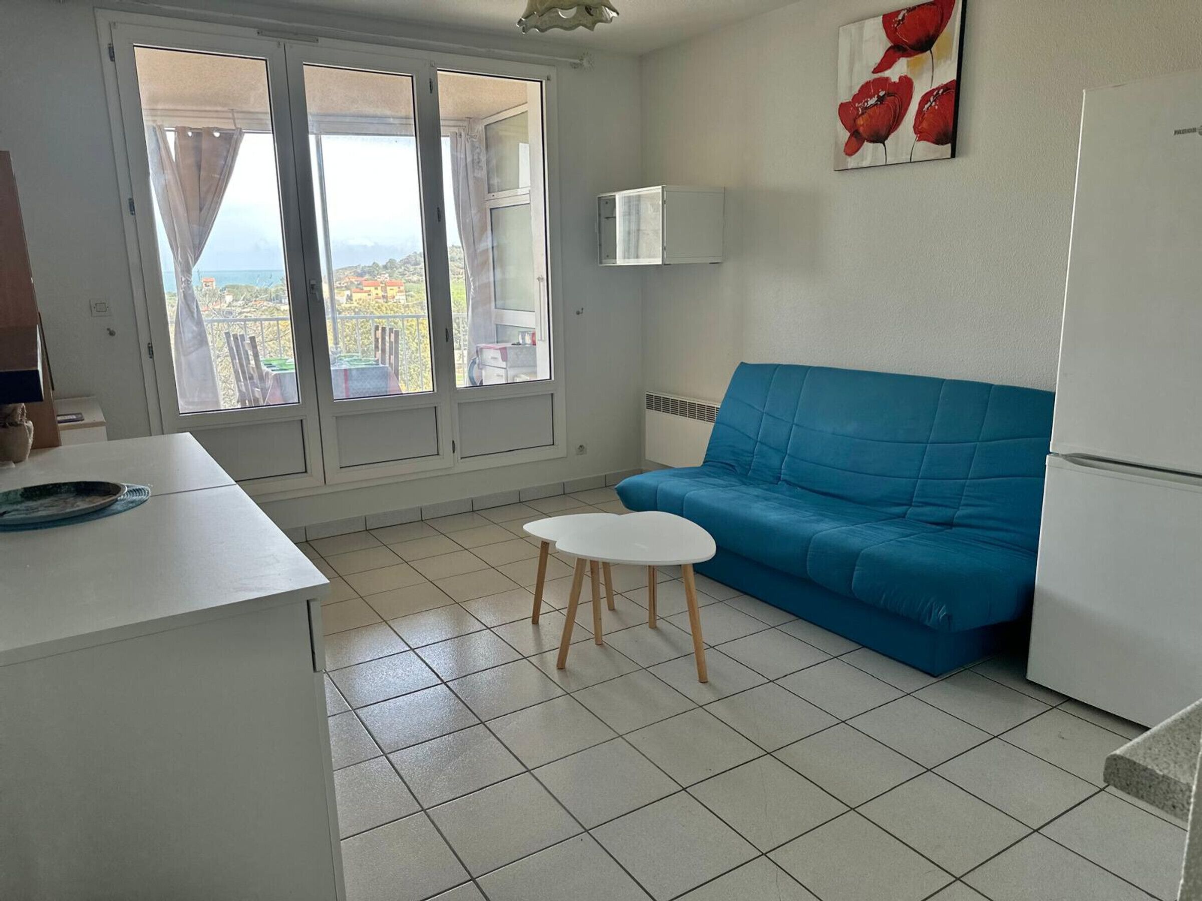 A small kitchenette with a white refrigerator, a blue sofa, and a small white table.