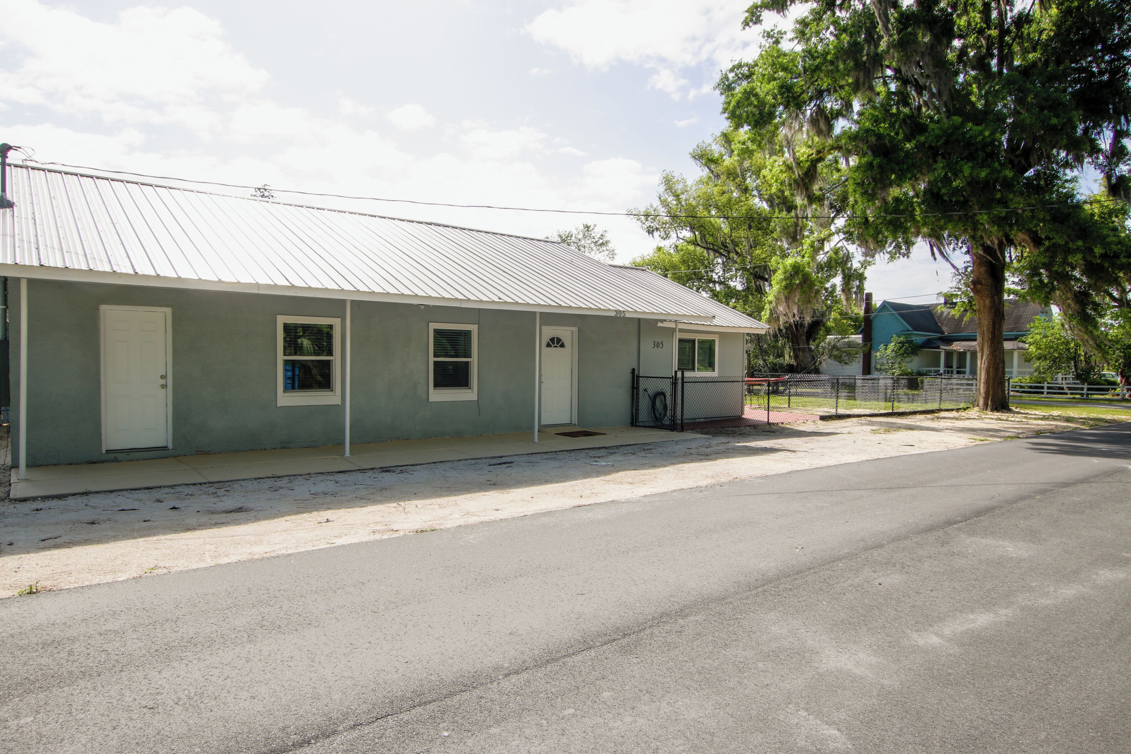 A single-story building with a metal roof, numbered doors, and a fenced area with a tree.