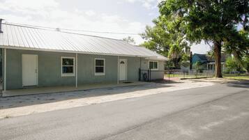 A single-story building with a metal roof, numbered doors, and a fenced area with a tree.