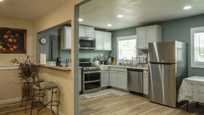 Una cocina con armarios blancos, electrodomésticos de acero inoxidable, un reloj y una planta.