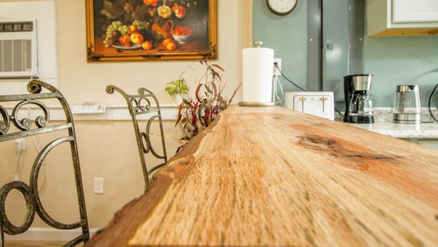 Una cocina con una mesa de madera, un cuadro, un reloj y un refrigerador.