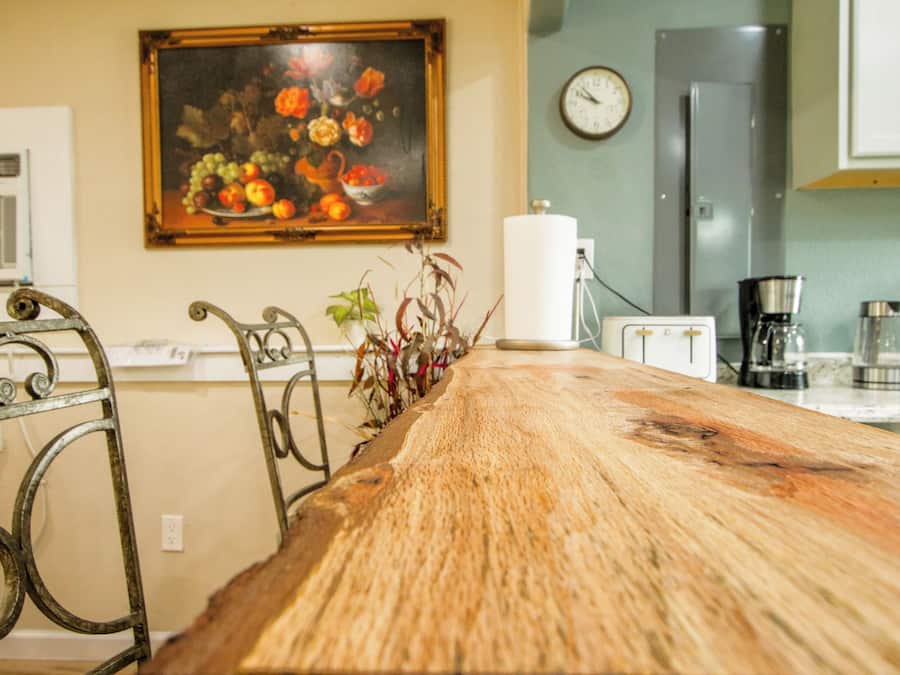 Uma cozinha com mesa de madeira, um quadro, um relógio e uma geladeira.