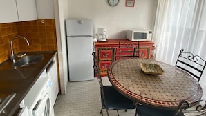Eine kompakte Küche mit Kühlschrank, Mikrowelle, Spüle und einem Essbereich mit rundem Tisch und Stühlen.