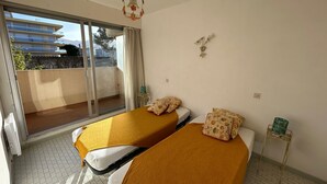 Ein Schlafzimmer mit zwei Betten, einem Fenster, einem Deckenventilator und einem kleinen Tisch.