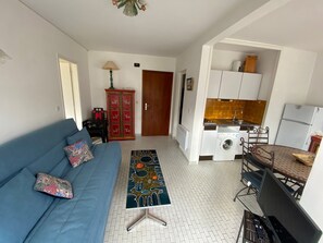 A living room with a sofa, a patterned rug, a washing machine, and a dining area. - Beachside apartment - 4 guests (Argelès-sur-Mer)
