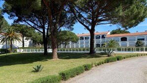 A paved pathway leading to a building with a red-tiled roof and arched windows, surrounded by a well-maintained lawn and trees. - Apartment near beach - 4 guests (Argelès-sur-Mer)