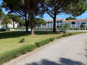 A paved pathway leading to a building with a red-tiled roof and arched windows, surrounded by a well-maintained lawn and trees. - Apartment near beach - 4 guests (Argelès-sur-Mer)