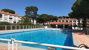 A swimming pool with a tiled deck, surrounded by buildings with arched windows and a clear sky. - Apartment near beach - 4 guests (Argelès-sur-Mer)