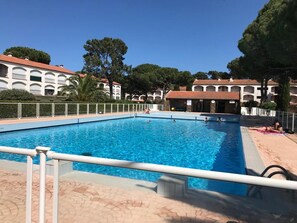 A swimming pool with a tiled deck, surrounded by buildings with arched windows and a clear sky. - Apartment near beach - 4 guests (Argelès-sur-Mer)