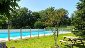 Una piscina cercada, rodeada de césped y árboles.