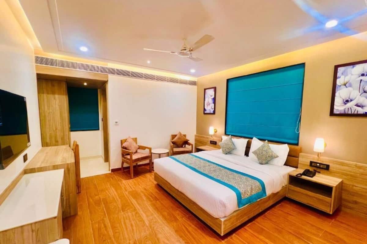 A hotel room with a bed, bedside tables, a desk, a chair, a ceiling fan, and a TV.