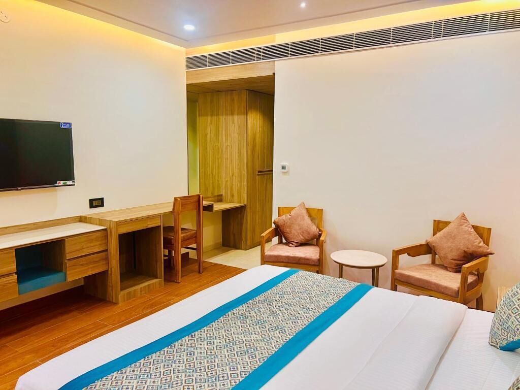 Een hotelkamer met een bed, een bureau, twee stoelen, een televisie en een houten kledingkast.