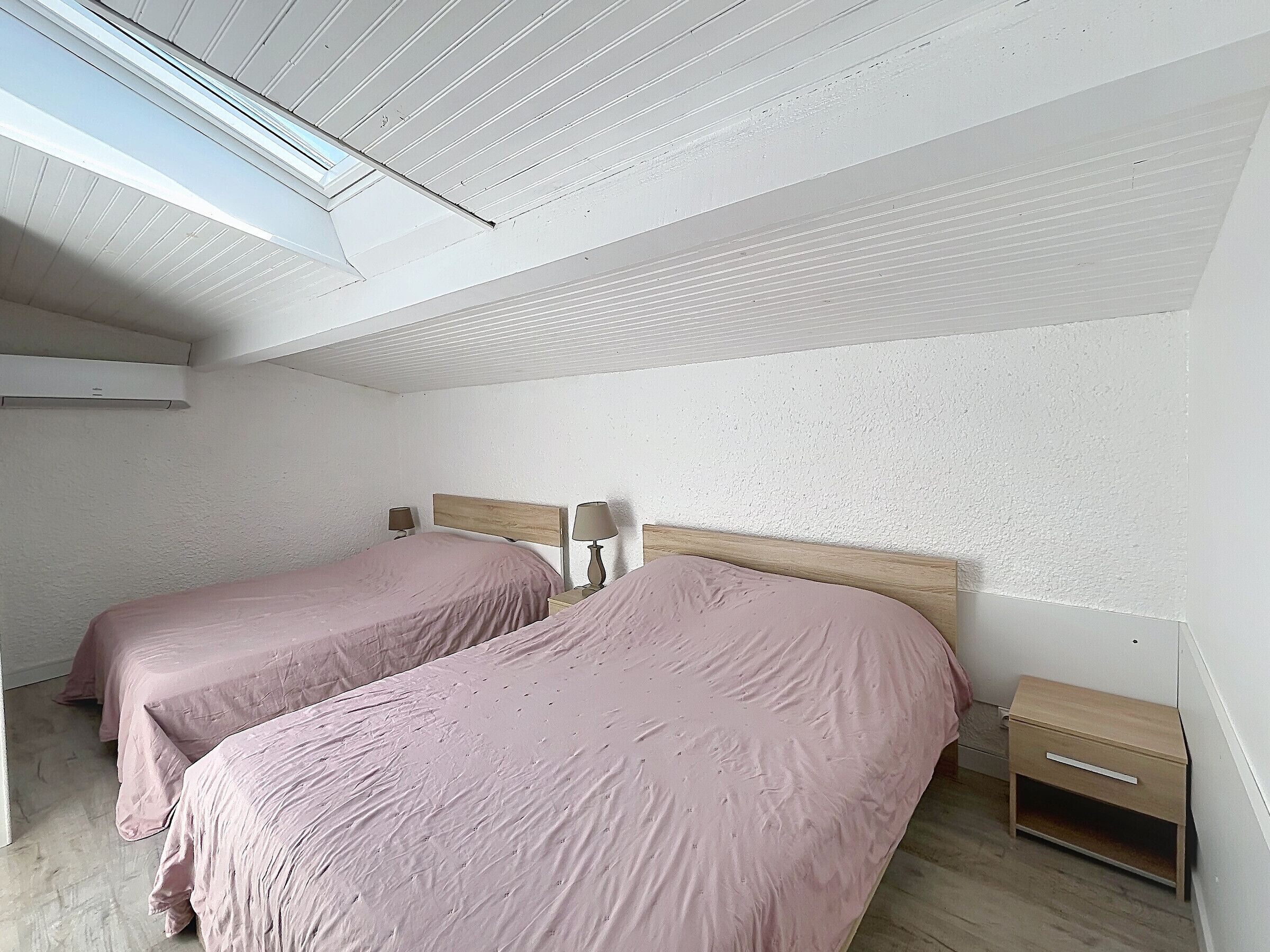 A bedroom with two beds, a skylight, a nightstand, and a wooden dresser.
