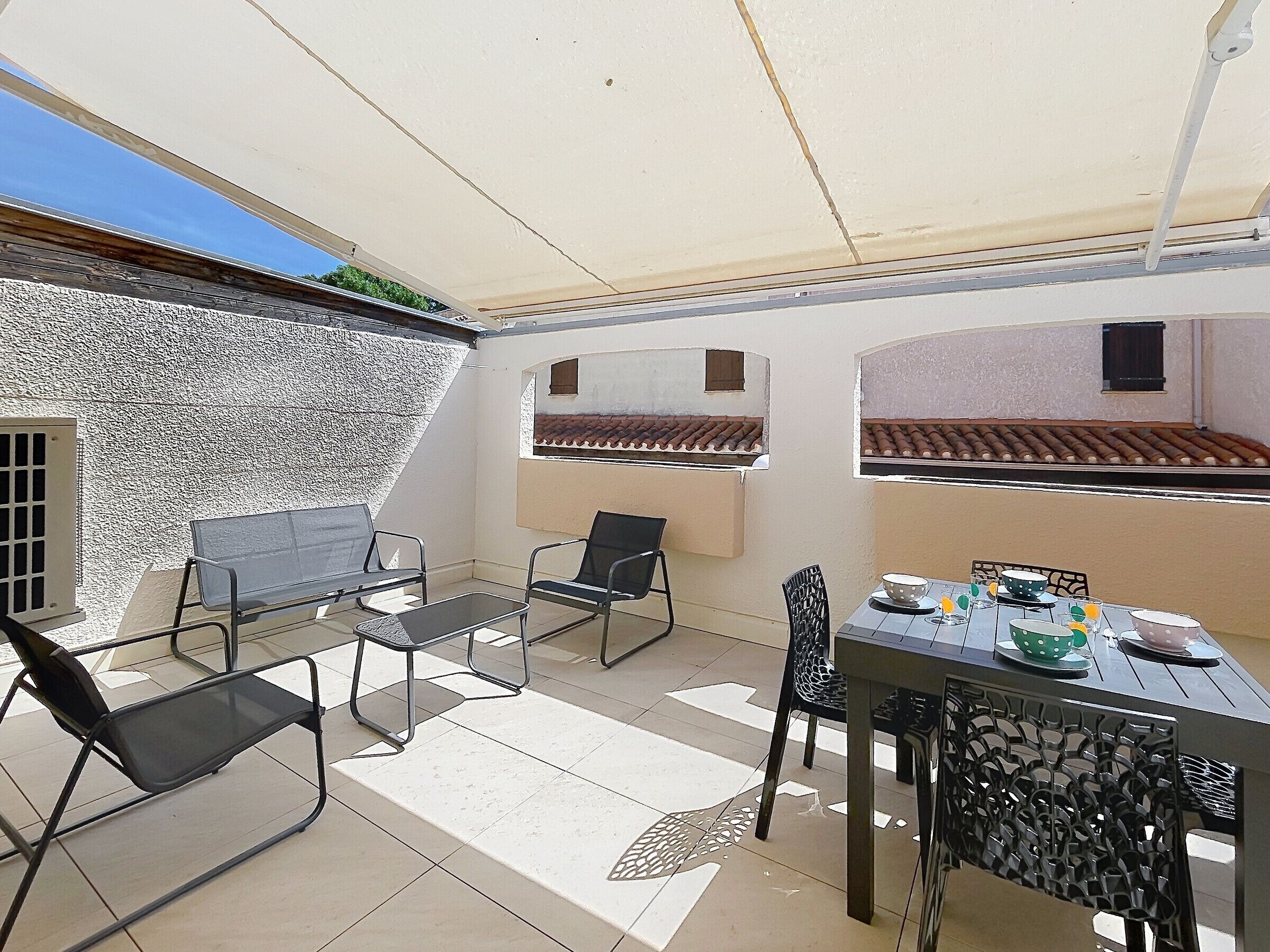Une terrasse extérieure avec une table dressée pour les repas, des chaises et un espace salon abrité.