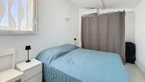 Ein Schlafzimmer mit einem Bett, einem Nachttisch, einer Lampe, einem Fenster mit Vorhängen und einer Tür.