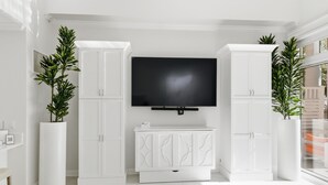 Una sala de estar moderna con televisor de pantalla plana, muebles blancos y plantas en macetas.