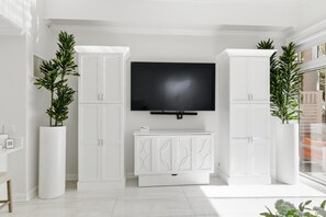 Ein modernes Wohnzimmer mit Flachbildfernseher, weißen Schränken und Topfpflanzen.