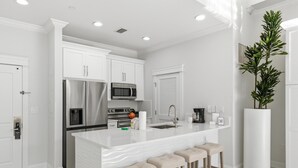 Cocina moderna con armarios blancos, electrodomésticos de acero inoxidable, una isla de mármol con taburetes y una planta en maceta.