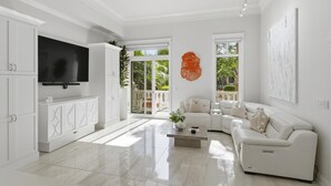 Una sala de estar moderna con un televisor de pantalla plana, sofás blancos, una mesa de centro y un ventanal con vistas a zonas verdes.