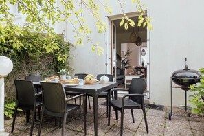 Une terrasse extérieure avec une table dressée pour le petit-déjeuner, entourée de chaises, et un barbecue.