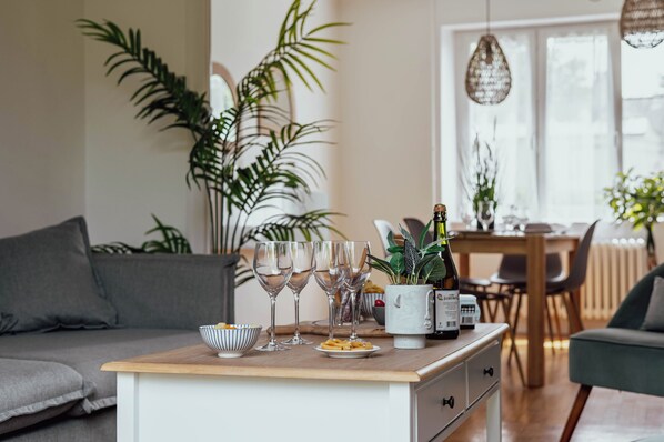 Un salon moderne avec un canapĂ©, une table basse sur laquelle se trouvent des verres et une bouteille, et un coin repas Ă lâarriĂšre-plan.