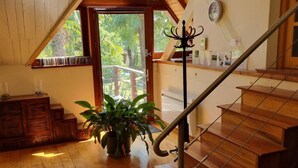 Una escalera de madera con barandilla de metal, un banco de madera y una planta en maceta en una habitación con suelo de madera y techo inclinado.