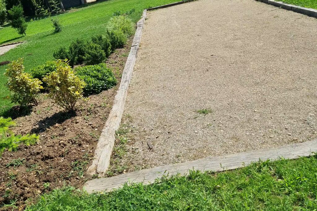 Een tuin met een grindpad, afgegrensd door een houten omheining.