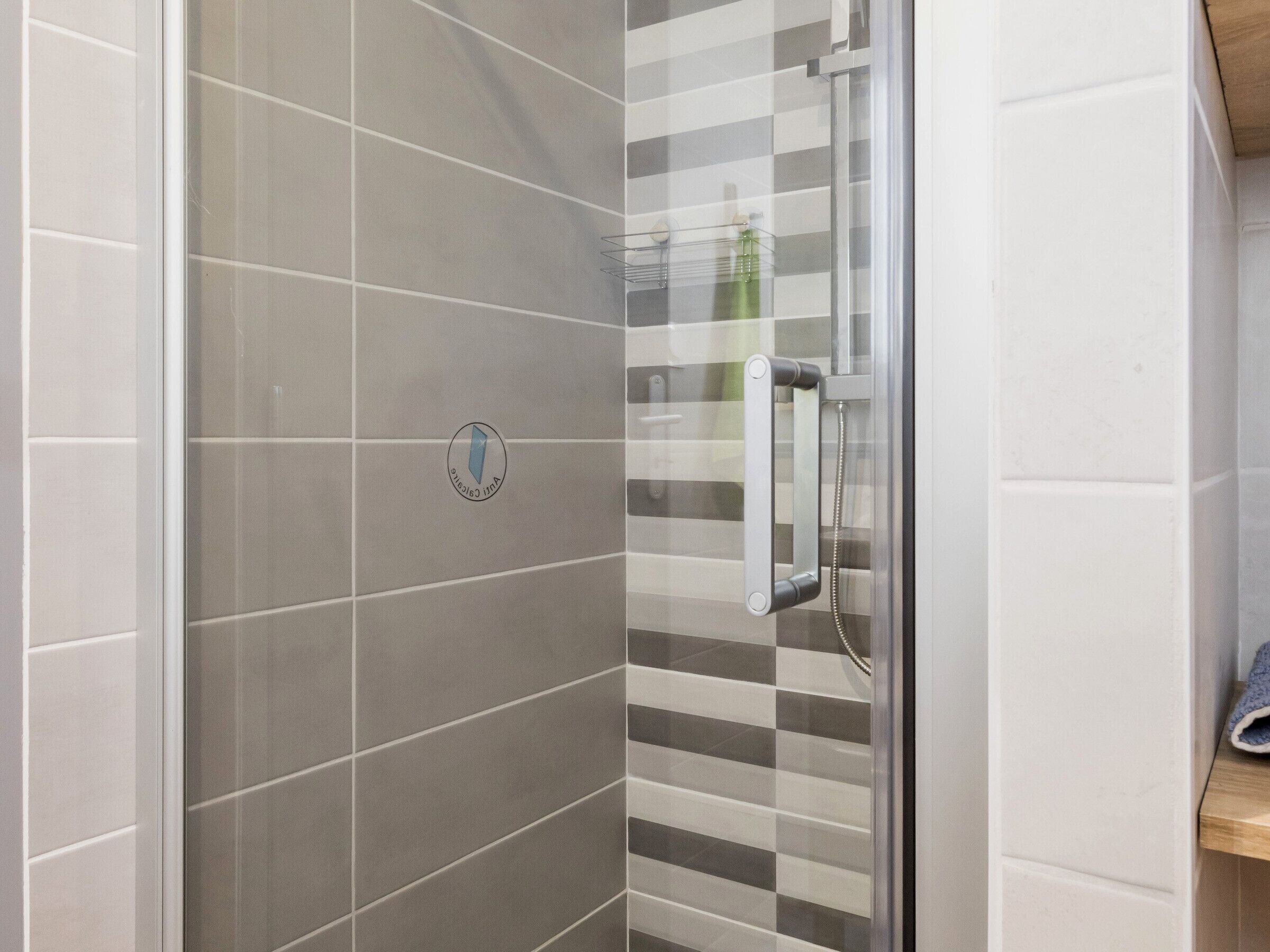 A shower with a glass door, a towel rack, and a logo on the wall.