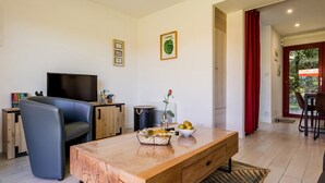 A modern living room with a wooden coffee table, a sofa, a TV, and a dining area with red curtains. - Peaceful cottage near Nantes - 4 guests (Ligné)