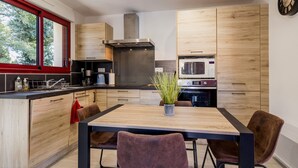 A modern kitchen with wooden cabinets, a stainless steel range hood, a microwave, and a dining area with a table and chairs. - Peaceful cottage near Nantes - 4 guests (Ligné)