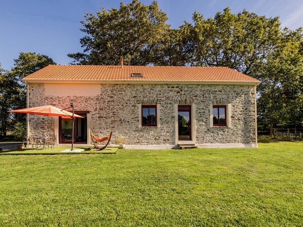 A stone house with a tiled roof, a patio with outdoor furniture, and a hammock.