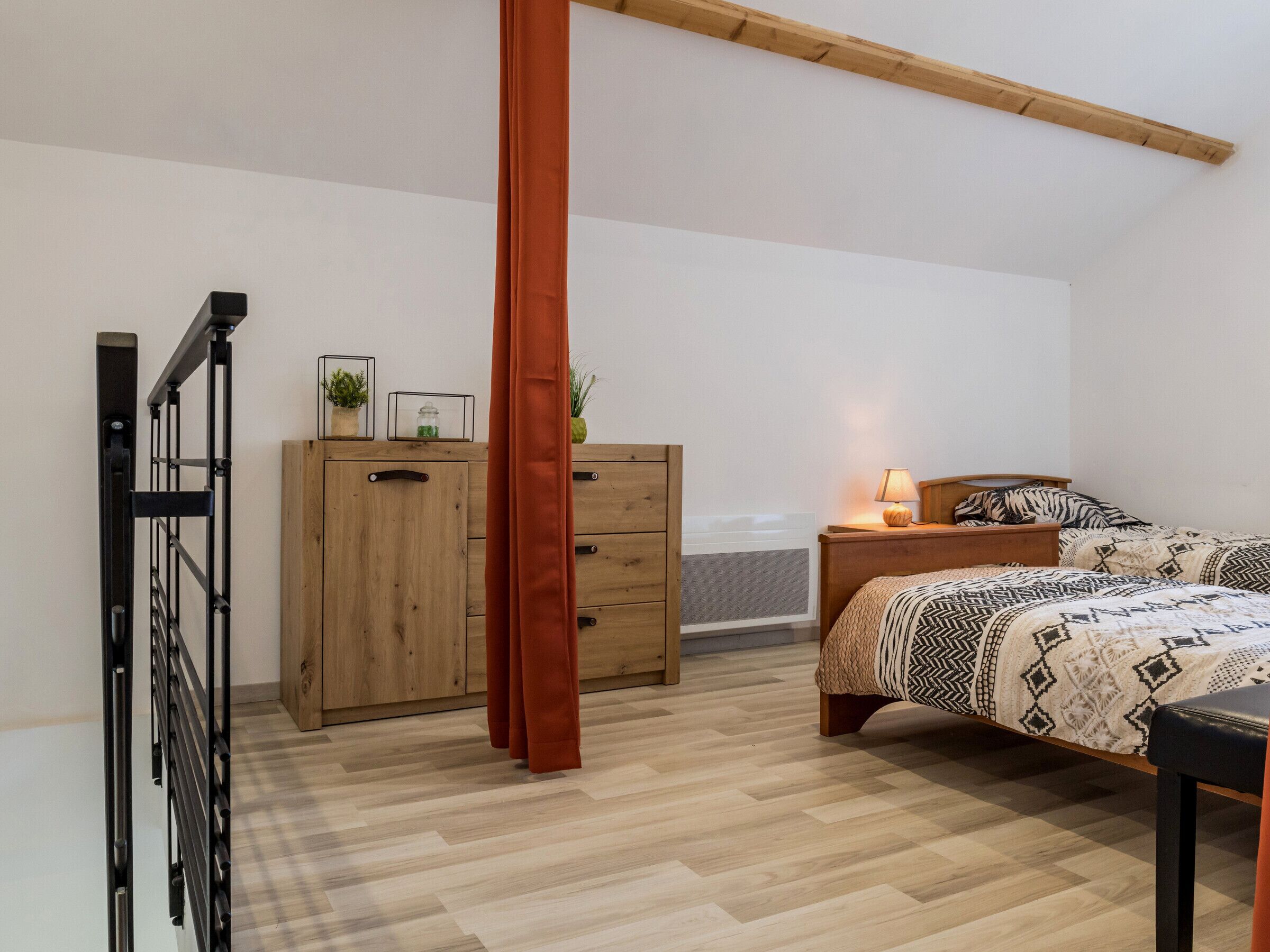 A bedroom with a bed, a wooden dresser, a nightstand with a lamp, and a metal rack.